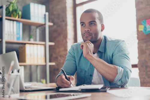 Skeptic, unsure, uncertain, doubts concept. Young african student is making decision sitting at the office in casual smart photo