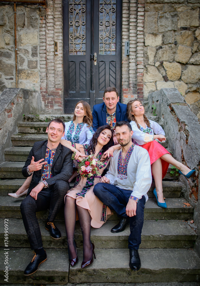 Fototapeta premium Pretty people in embroidred clothes sit before old stone building