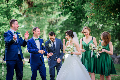 Newlyweds, groomsmen and bridesmaids pose together in a summer park