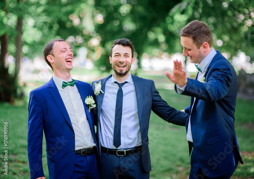Groom and groomsmen in blue suits pose together in green park