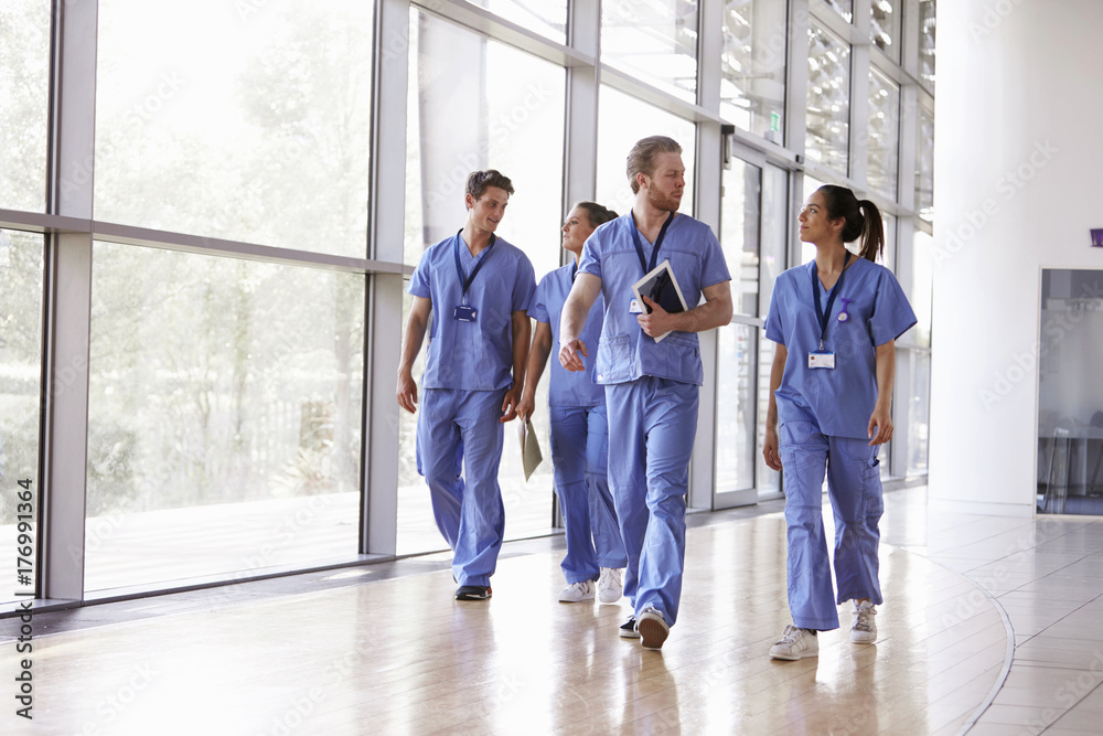 Four healthcare workers in scrubs walking in corridor Four healthcare workers in scrubs walking in corridor