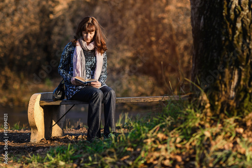red-haired woman sitting on bench in park and reading book