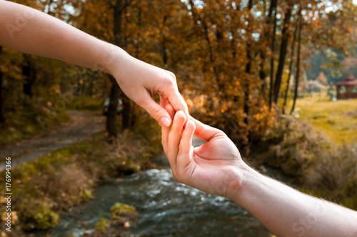 A man's hand easily holds a woman's hand against the backdrop of an autumn landscape © Bogdan