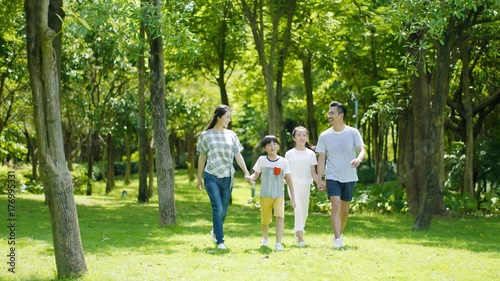asian family of 4 walking & laughing in park in sunny summer in slow motion
