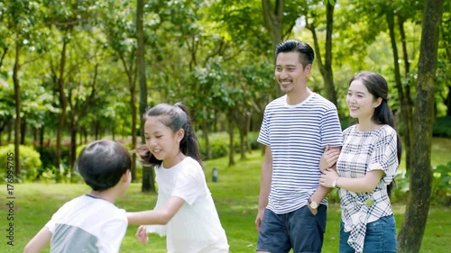 asian family of 4 walking & laughing in park in sunny summer in sow motion