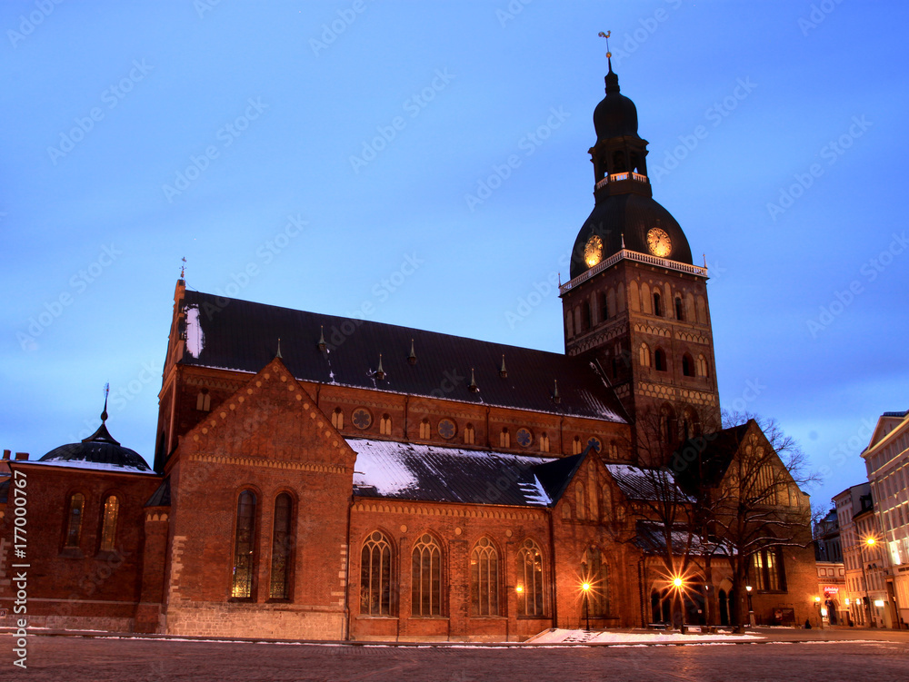 Riga, Latvia. View Of Dome Square And Dome Cathedral In Evening Illumination Under Blue Sky. Winter time, first snow