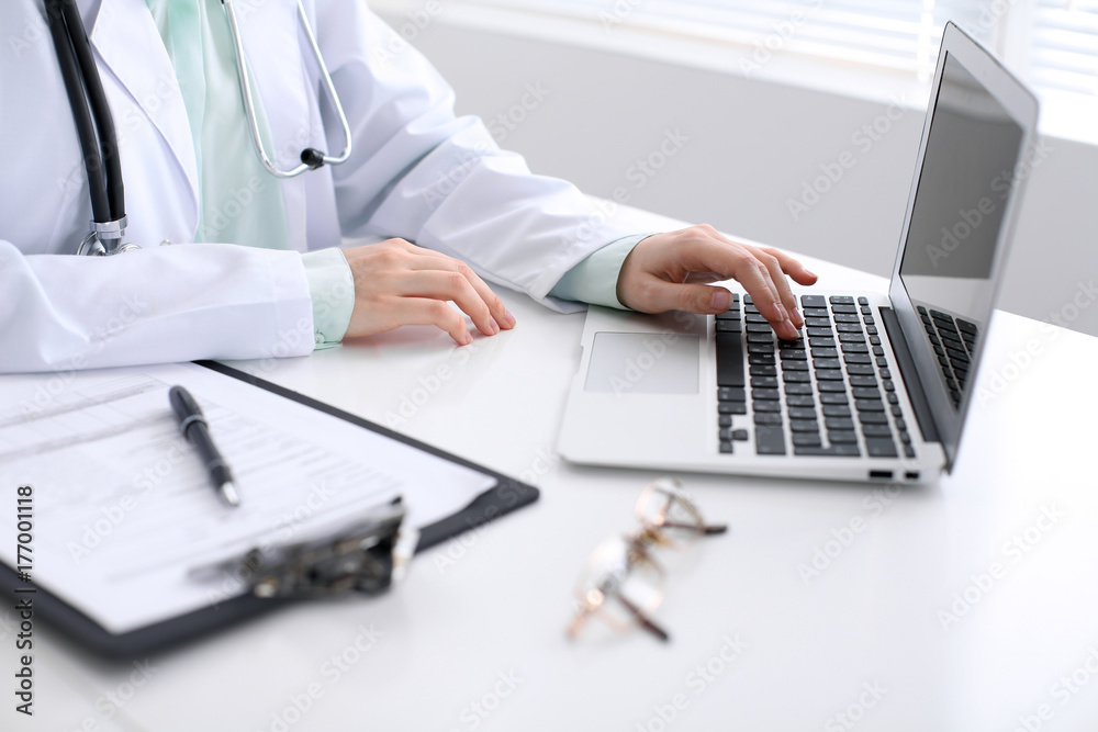 Close-up of a female doctor typing on laptop computer, sitting at the table in the hospital Close-up of a female doctor typing on laptop computer, sitting at the table in the hospital