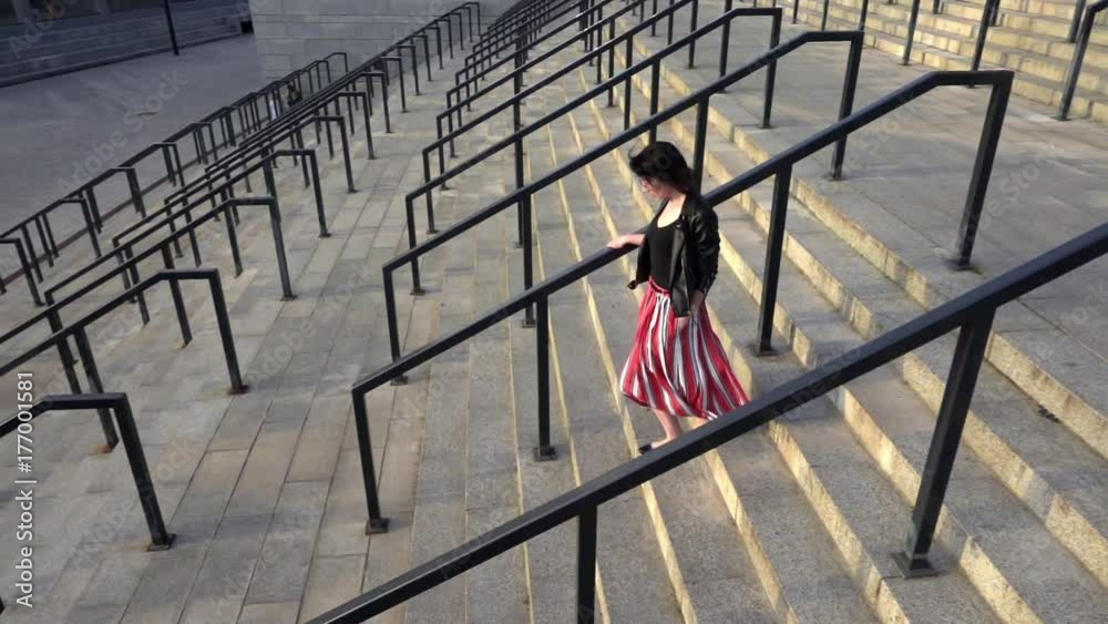 Beautiful brunette woman in red striped pleated skirt is running downstairs in slow motion. City life urban people behavior. The skirt and her hair are fluttering in the wind. High angle overhead. Beautiful brunette woman in red striped pleated skirt is running downstairs in slow motion. City life urban people behavior. The skirt and her hair are fluttering in the wind. High angle overhead.