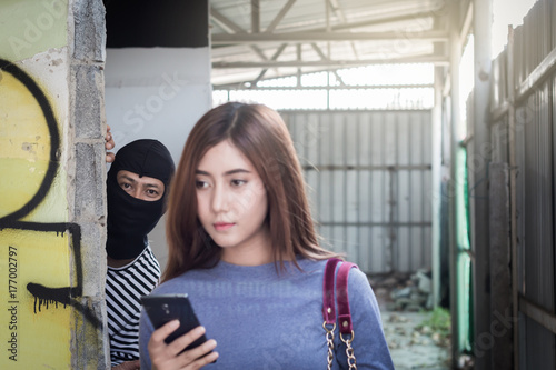 Beautiful young woman holding smartphone and being stalked by man criminal with the knife