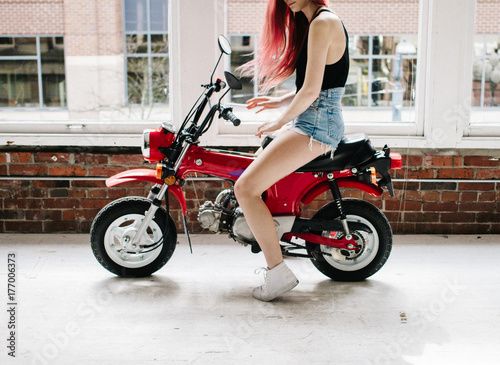 young attractive female with denim shorts on small motorbike scooter indoors