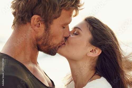 Closeup portrait of romantic young couple kissing at the beach photo