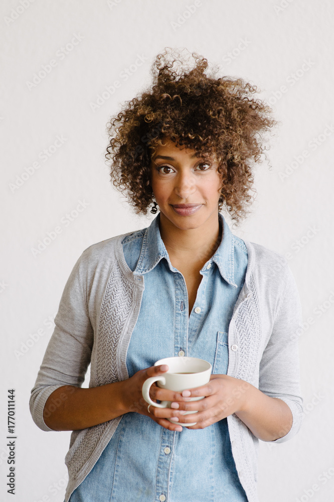 A women stands holding a cup of coffee while looking at the camera. A women stands holding a cup of coffee while looking at the camera.