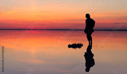 Silhouette of alone man looking toward vibrant sunset reflected in shallow waters of solt lake