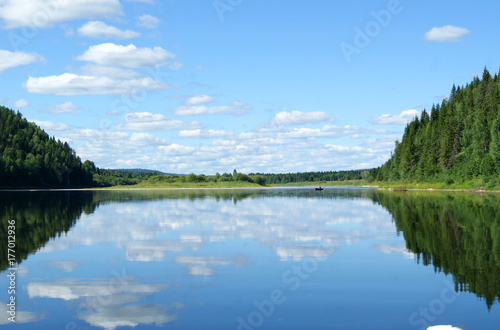 Fototapeta Naklejka Na Ścianę i Meble -  landscape: the Ural river Vishera in clear weather, the calm water reflects the wooded shore and the sky with clouds..