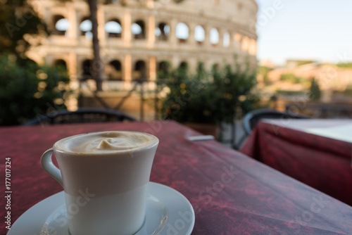 Italian cappuccino coffee cup on a table, with roman coliseum in background, at sunrise in Rome, Italy