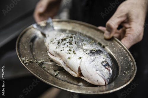 Chef holding roasting tray with raw seasoned sea bream fish