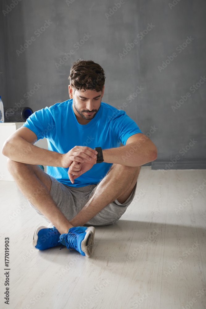 Burn calories. Handsome young man checking his smart watch while sitting at the gym. Burn calories. Handsome young man checking his smart watch while sitting at the gym.