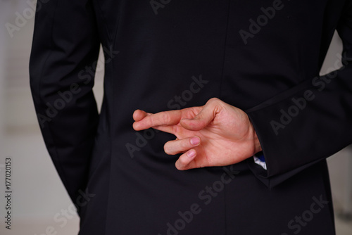 Close up of man wearing a suit, and crossing his fingers, in a blurred background