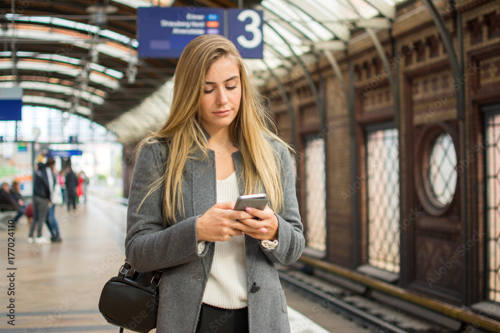Fototapeta premium Young woman using phone at train station.