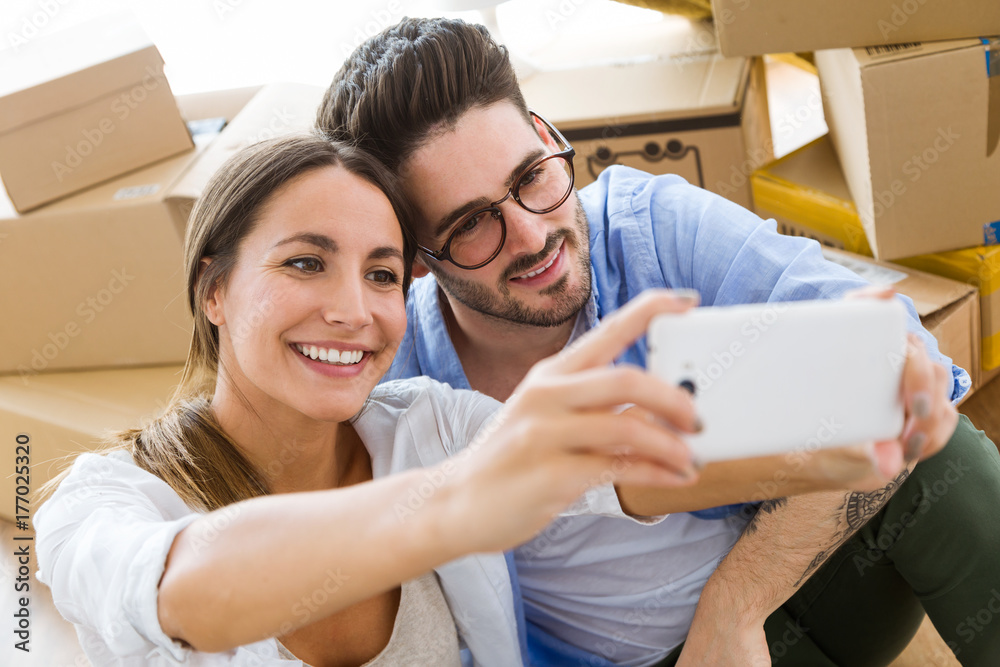 Beautiful young couple using mobile phone in their new home. Beautiful young couple using mobile phone in their new home.
