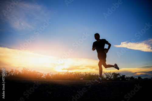 Fototapeta Naklejka Na Ścianę i Meble -  Young man running on a rural road during between the summer on vacation, run for health according nature on a rural, Early in the morning or before sunset.