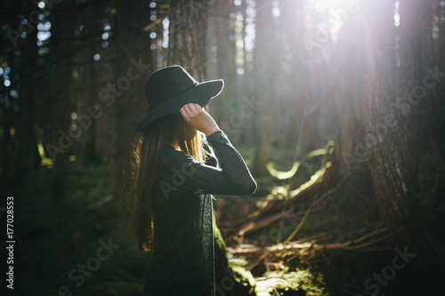 Girl adjusts hat under the sun in forest photo