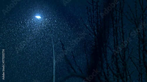 Night time snowfall in a city on peaceful, calm, tranquil evening during winter holidays season on streets of residential suburbs with houses, lights and cars covered with snow by thick snowflakes