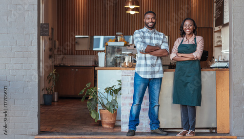 Two smiling African entrepreneurs standing in front of their cafe © mavoimages