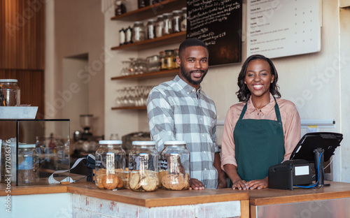 Two smiling African entrepreneurs standing behind their cafe counter