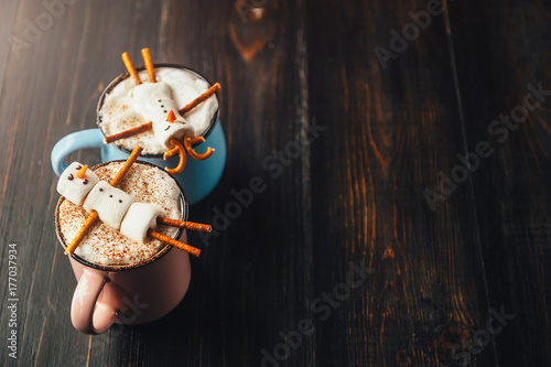 a mug with hot chocolate on a wooden table with a marshmallow man who is resting in a mug photo