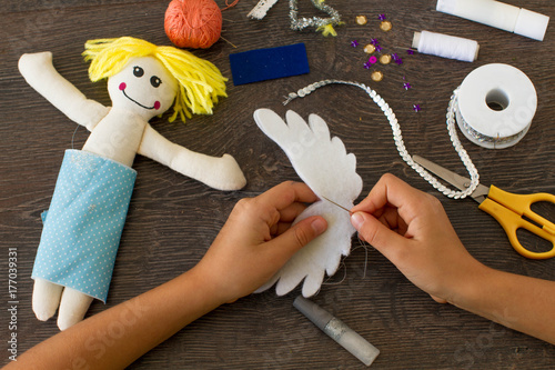 Child making a felt angel doll with sewing supplies on wooden table. photo