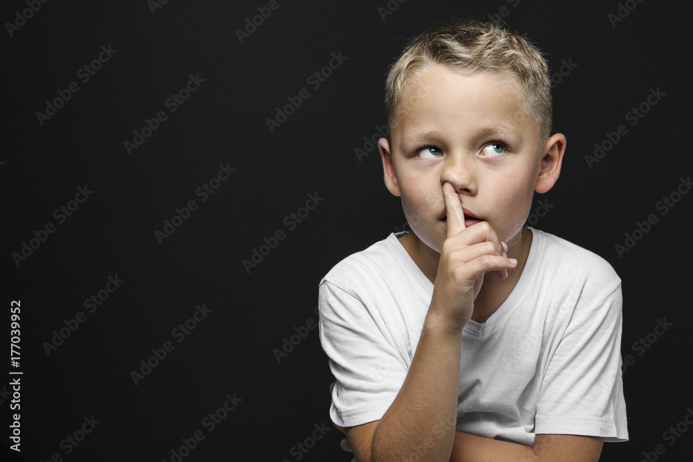 little blond boy thinks and drills with the pointing finger in the nose