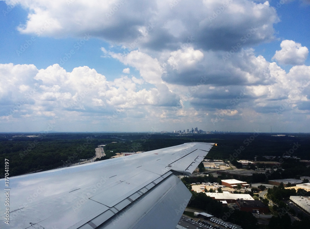 City skyline in the distance on the tip of the wing of an airplane flying over warehouses