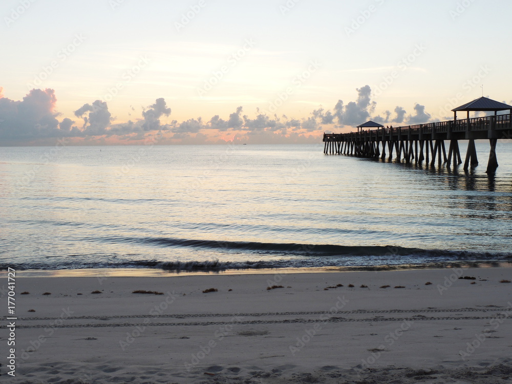 Obraz premium Watching the sunset and waves crashing on the beach next to a pier