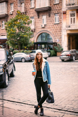 young stylish red hair girl, passing by the Windows.Wearing fashionable glasses and a black coat.Keeps coffee.Abstract looking to the side. concept of street fashion © chichkaua