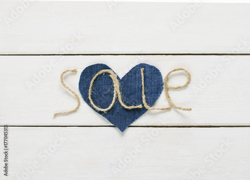  inscription sale of twine in my hand on a denim heart on white wooden background for storefront design