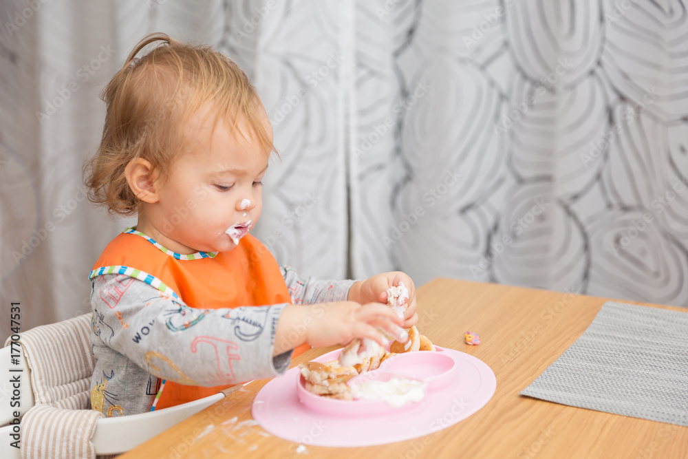 One and a half year old baby girl feeding herself with her fingers, baby led weaning; concept of motherhood and parenting One and a half year old baby girl feeding herself with her fingers, baby led weaning; concept of motherhood and parenting