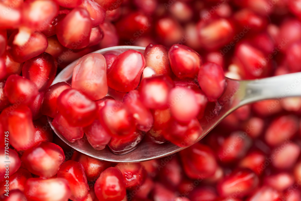 Spoon full of pomegranate seeds above the bowl of fruit, focus on spoon Spoon full of pomegranate seeds above the bowl of fruit, focus on spoon