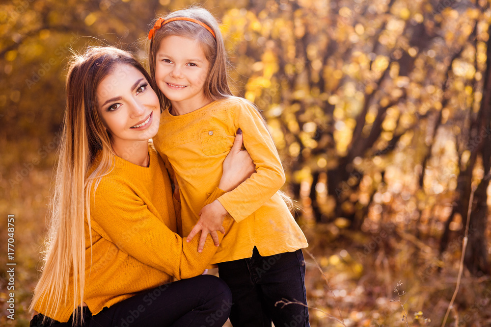 Portrait of happy smiling mother and daughter in yellow pullovers in the autumn park. Happy family outdoors. Autumn park. Leaf fall. Portrait of happy smiling mother and daughter in yellow pullovers in the autumn park. Happy family outdoors. Autumn park. Leaf fall.