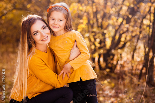 Portrait of happy smiling mother and daughter in yellow pullovers in the autumn park. Happy family outdoors. Autumn park. Leaf fall.