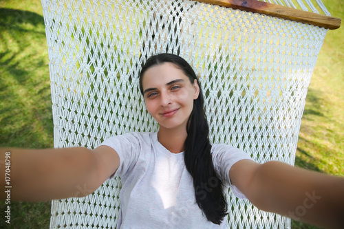 Woman lying on hammock and making selfie photo on smartphone outdoors