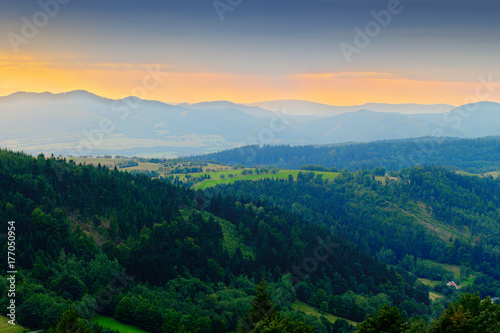 Vast panorama view of foggy valley in the Owl Mountains with silhouette of Sudetes mountain range at dusk. Mountainous countryside landscape in south-west Poland.