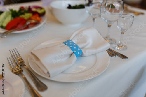 White napkin with ribbon on a white plate. Elegant decoration of table in a restaurant Decorated table for a celebration, wedding or anniversary.