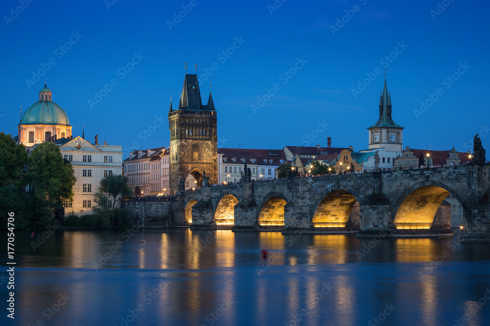 Naklejka premium Lit Charles Bridge (Karluv most) and old buildings at the Old Town and their reflections on the Vltava River in Prague, Czech Republic, at dusk.