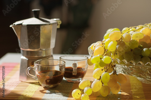 Still life branch of ripe grapes, two cups of coffee and a coffee maker