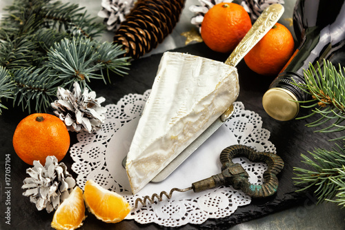 Brie cheese tangerines and fir twigs a bottle of wine and a corkscrew on a white Lacy napkin. Goodies for the holiday of Christmas and New year.