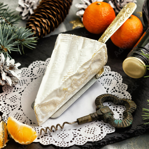Brie cheese tangerines and fir twigs a bottle of wine and a corkscrew on a white Lacy napkin. Goodies for the holiday of Christmas and New year.