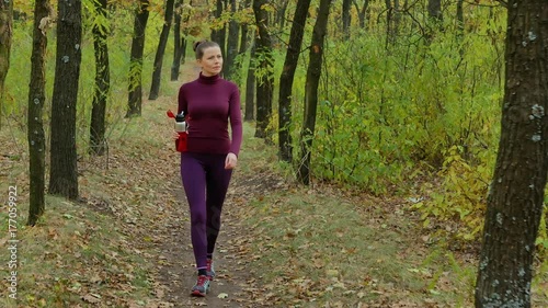 Beautiful fitness sport girl walking along the autumn park in sportswear with sports water bottle or isotonic drink in hand. photo