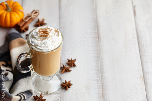 Fall pumpkin spice latte with whipped cream and cinnamon, ornamental pumpkins and warm woolen scarf on white wooden background, copyspace