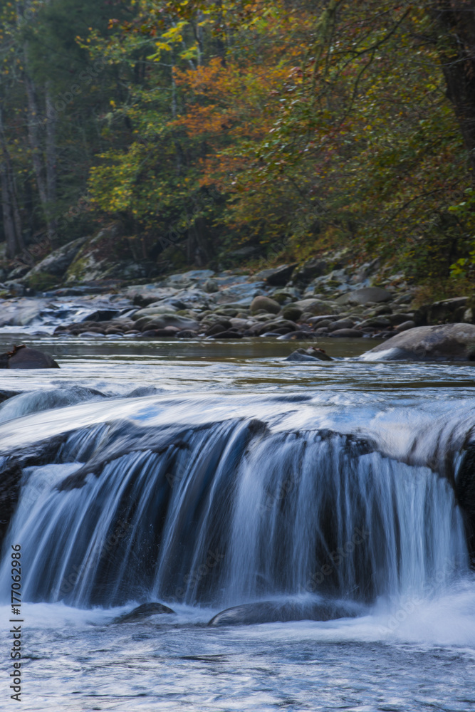Fototapeta premium Smooth flowing water falling over rocks downstream in forested environment landscape scene